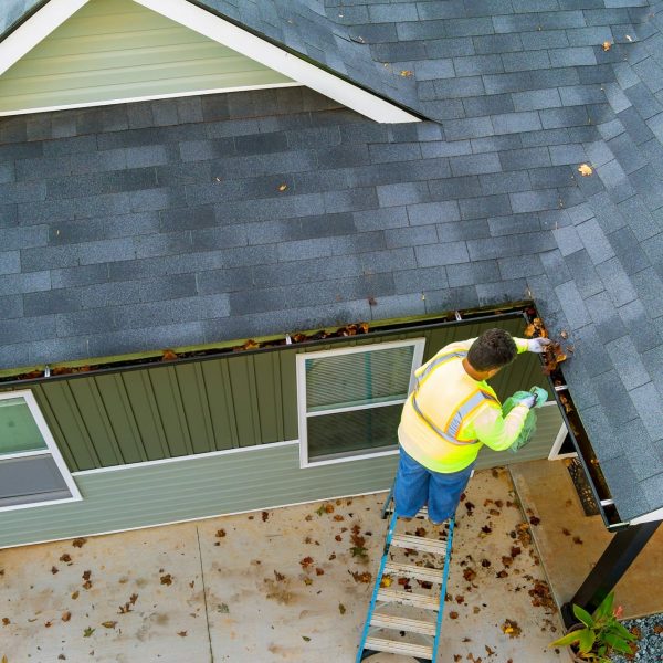 A worker is cleaning clogs in roof gutter drain by picking up dirt, debris, fallen leaves